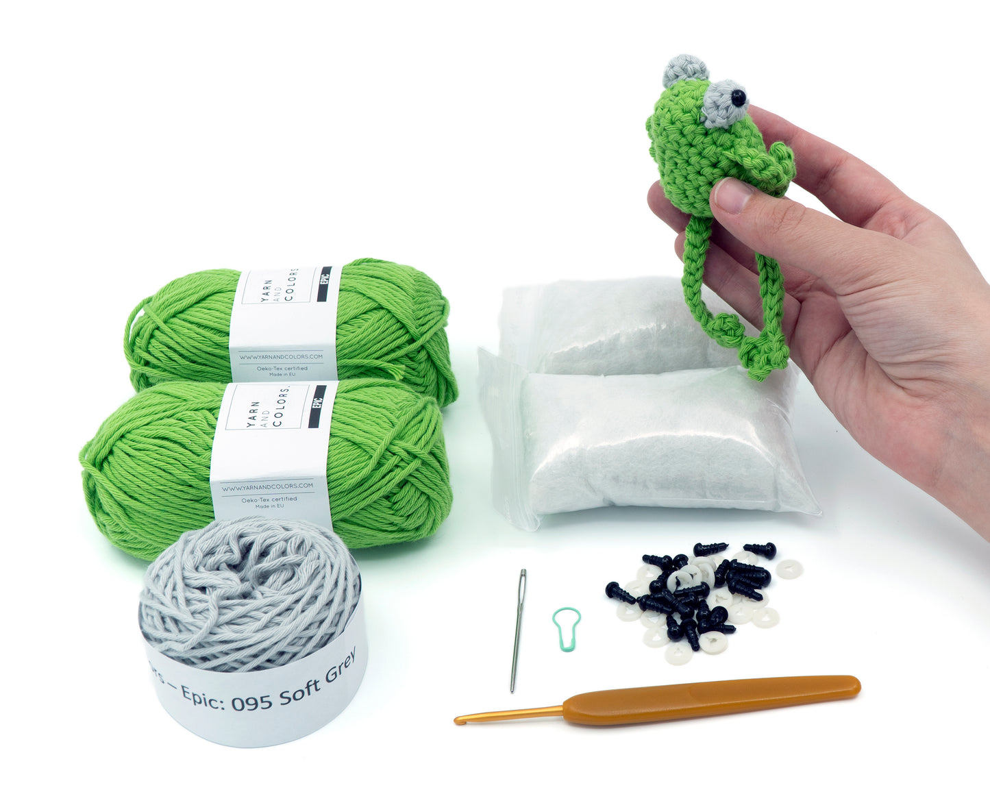 amigurumi crochet sitting frog kit completed frog being held in front of kit's contents