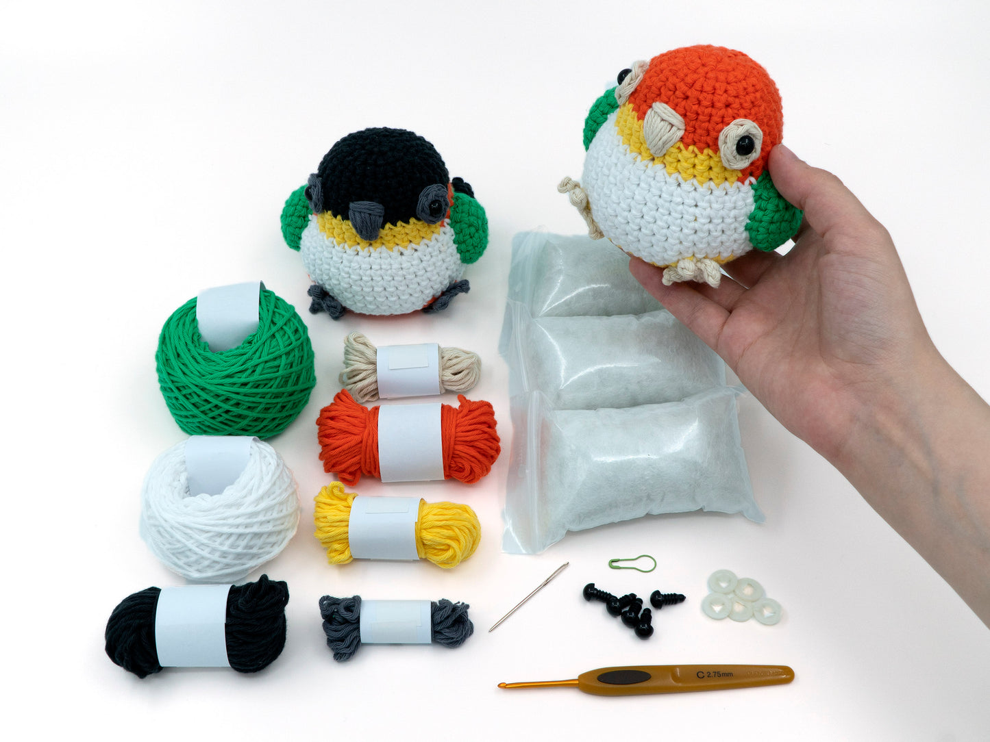 amigurumi crochet caique kit parrot in hand above the kit to show size comparison
