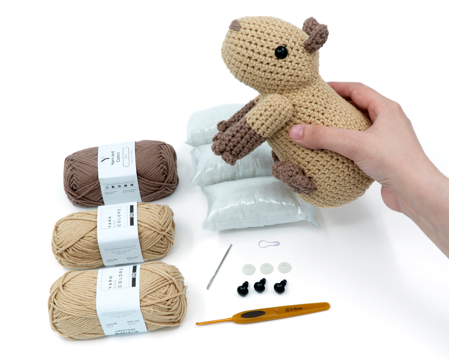 amigurumi crochet capybara kit with capybara in hand above the kit for size comparison