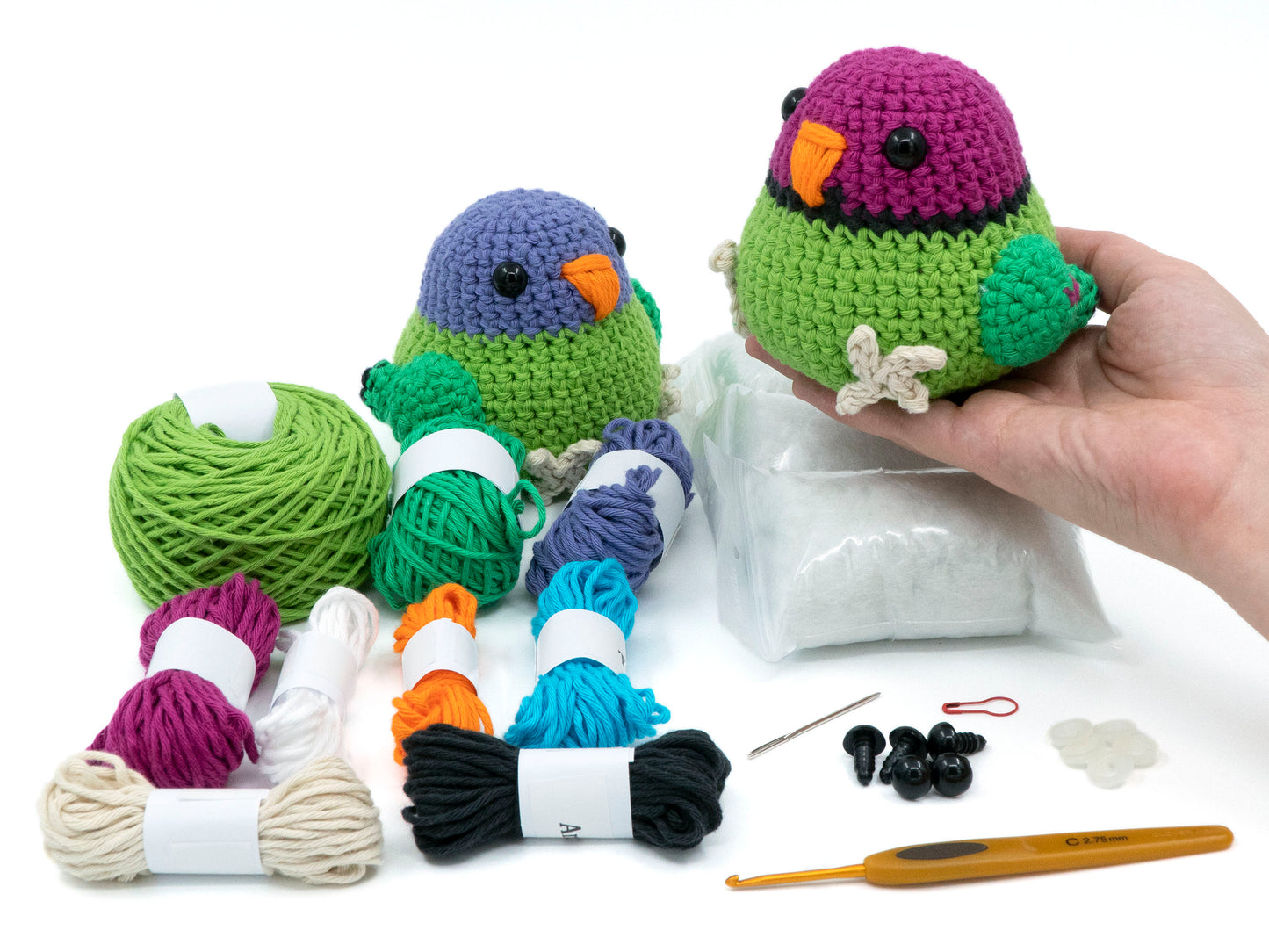 amigurumi crochet plum-headed parakeet kit a parrot being held above the crochet kit contents