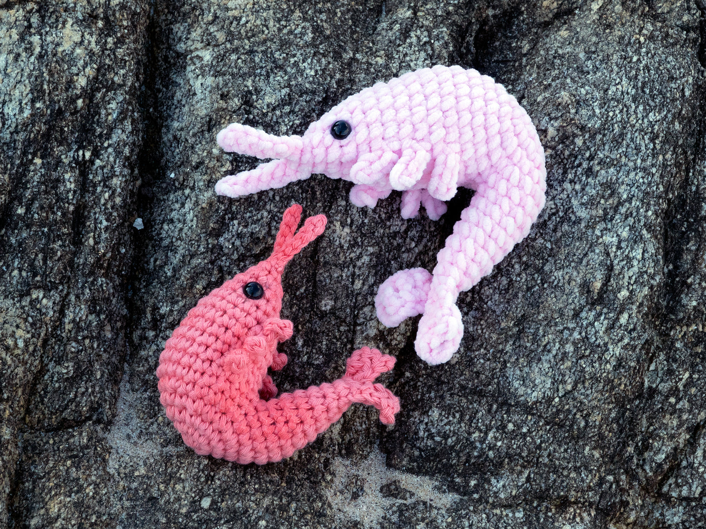 two amigurumi prawns sitting on a rock on the beach