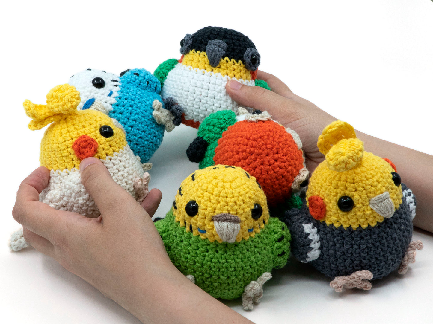 amigurumi crochet parrot pattern bundle with cockatiel budgie and caique being held for size comparison