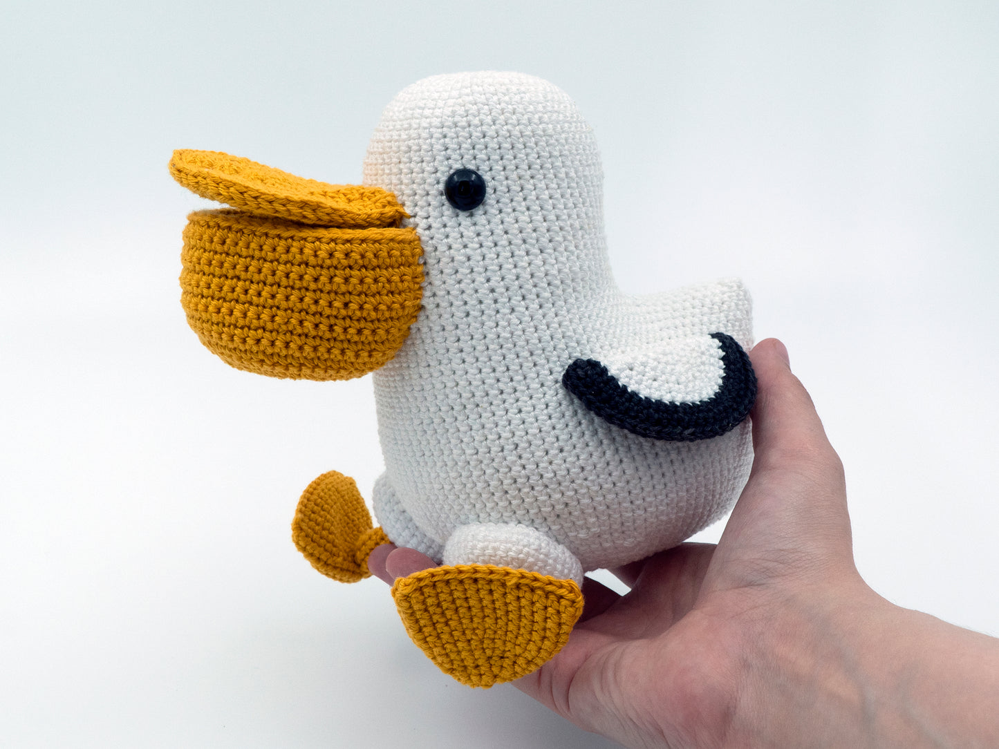 a crochet pelican bird sitting in a hand for scale