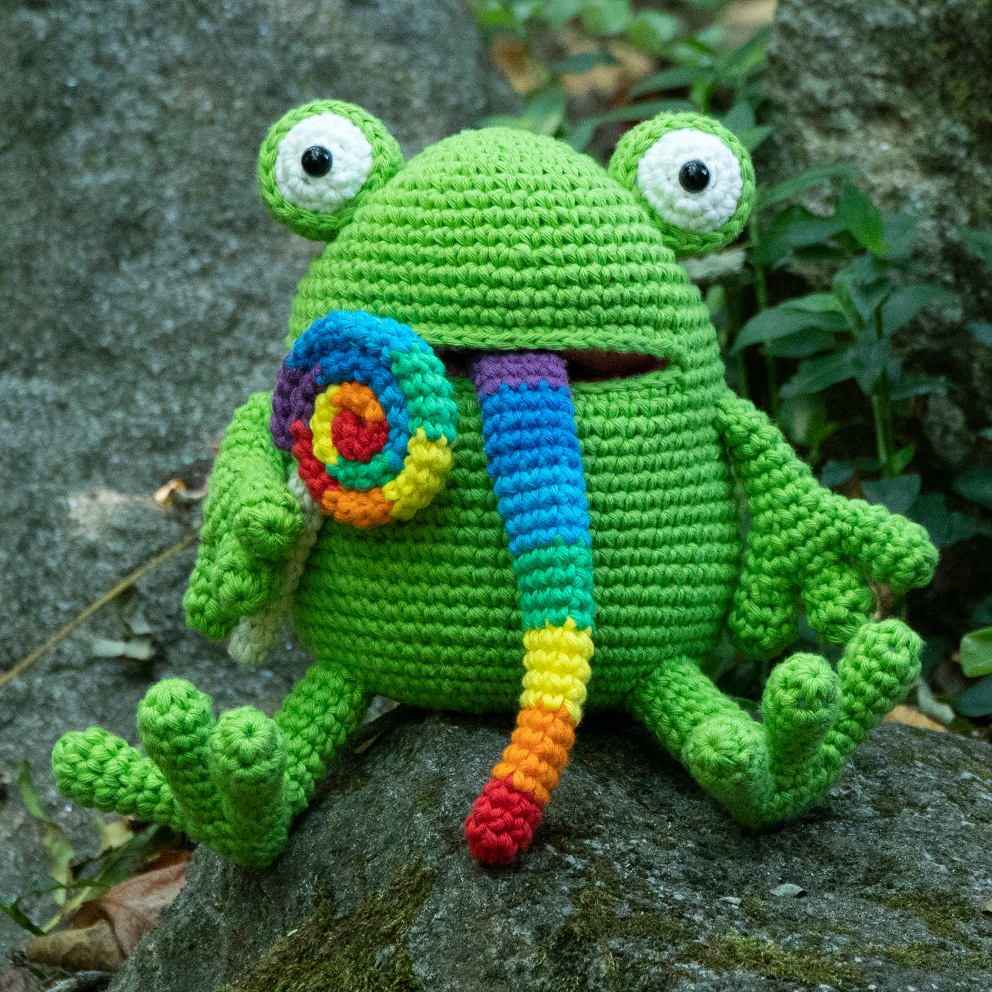 amigurumi frog eating a rainbow swirled lollipop