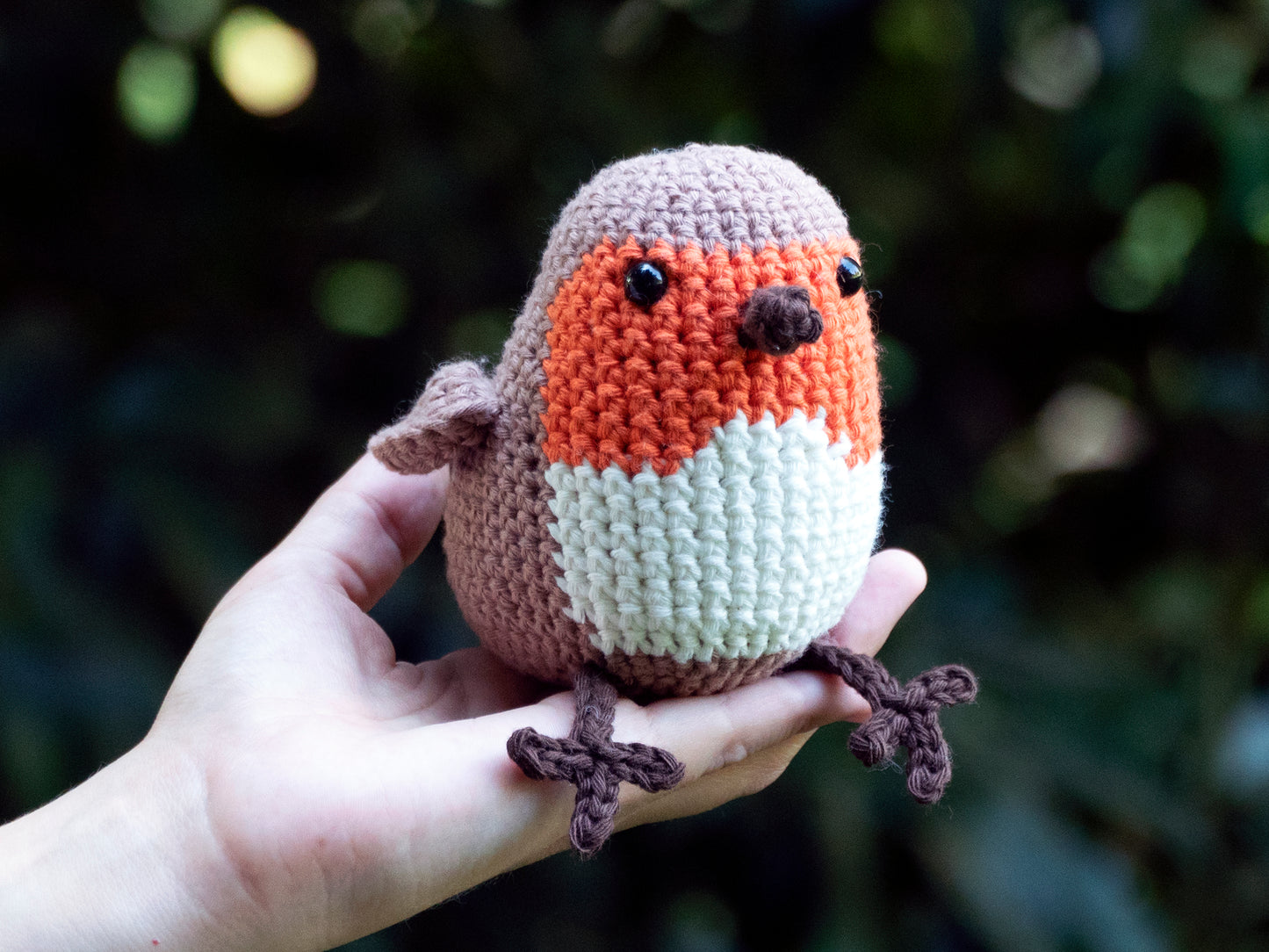 orange amigurumi crochet robin songbird sitting on a hand outside