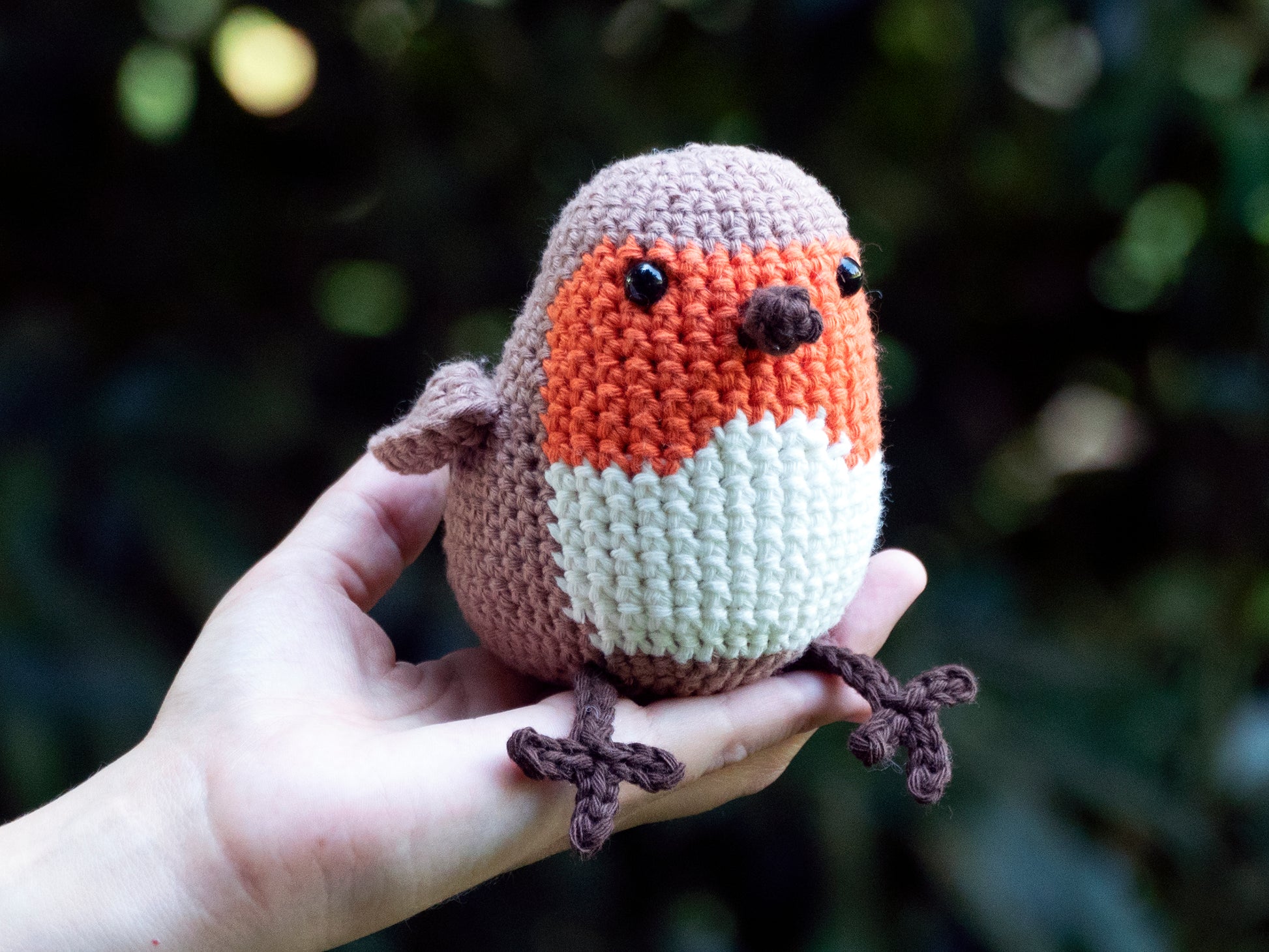 orange amigurumi crochet robin songbird sitting on a hand outside