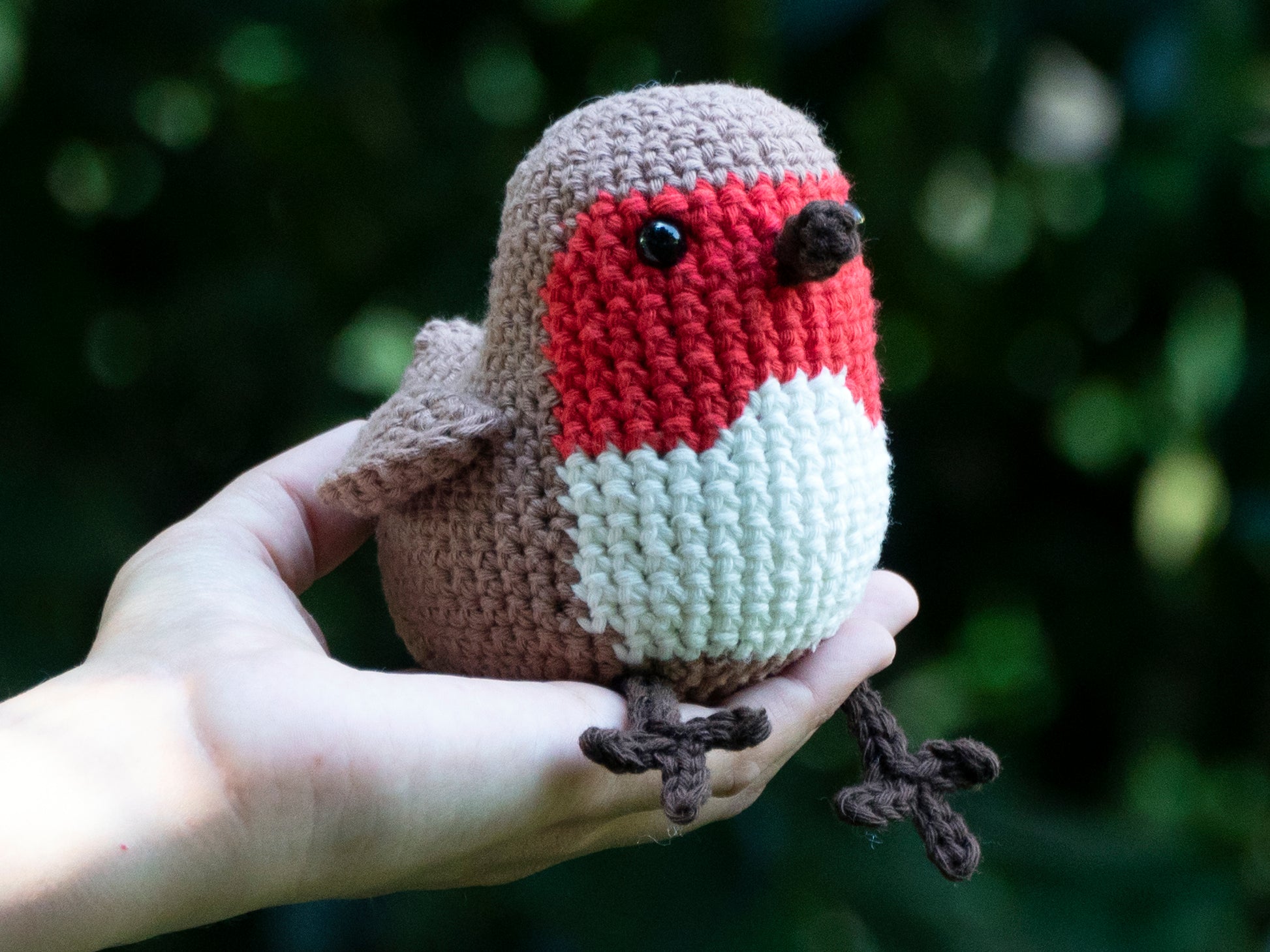 red amigurum crochet robin songbird sitting on a hand outside