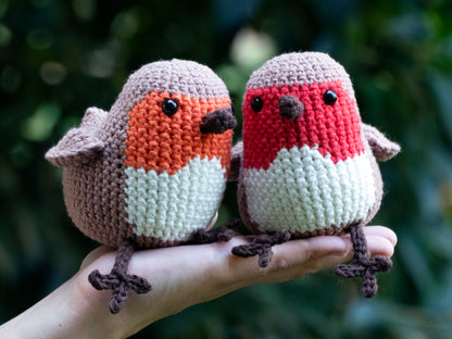 amigurumi crochet robin songbirds sitting on a hand facing each other outside for size comparison