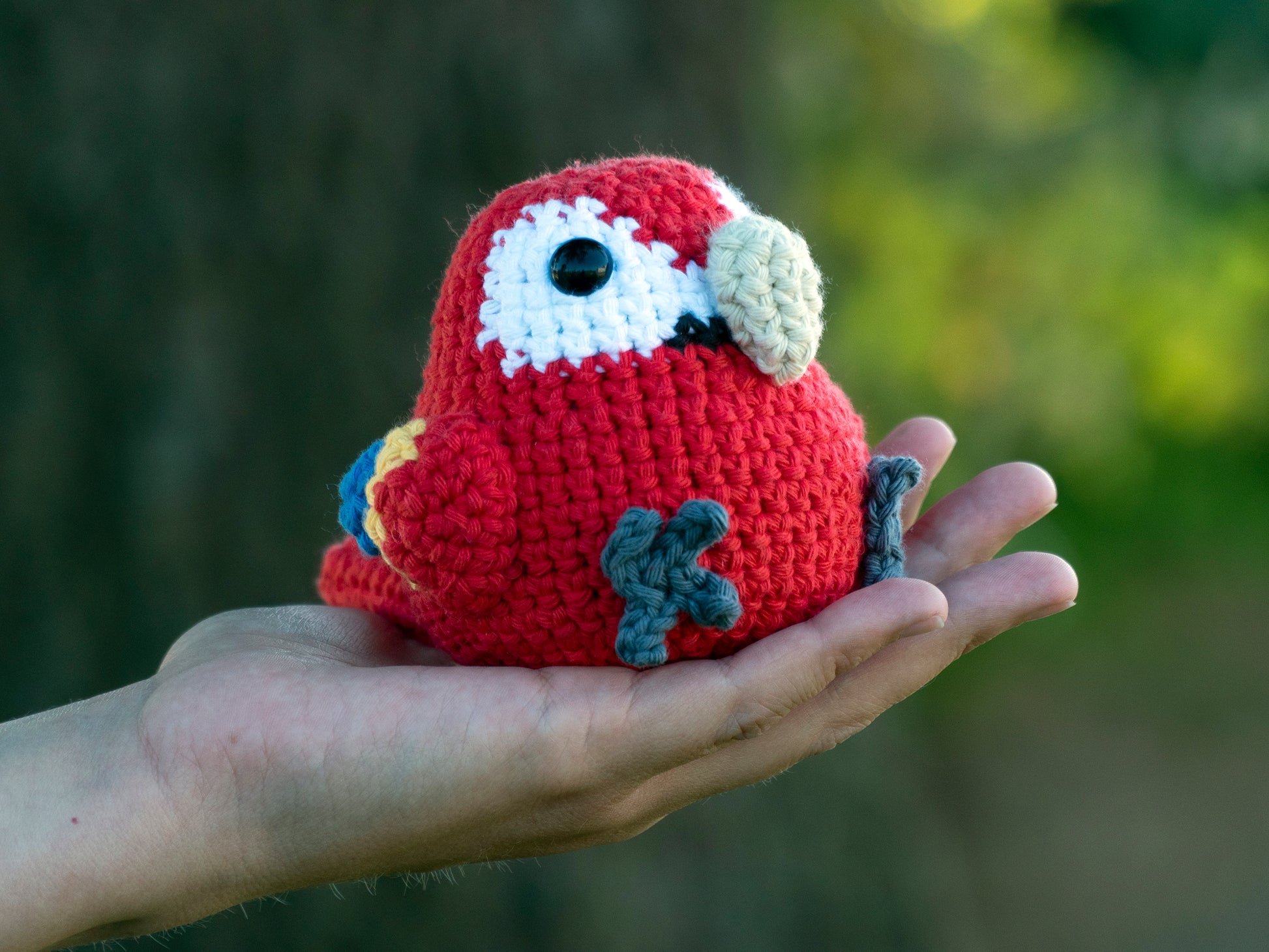 handmade crochet scarlet macaw amigurumi plush with crocheted beak being picked up for size comparison
