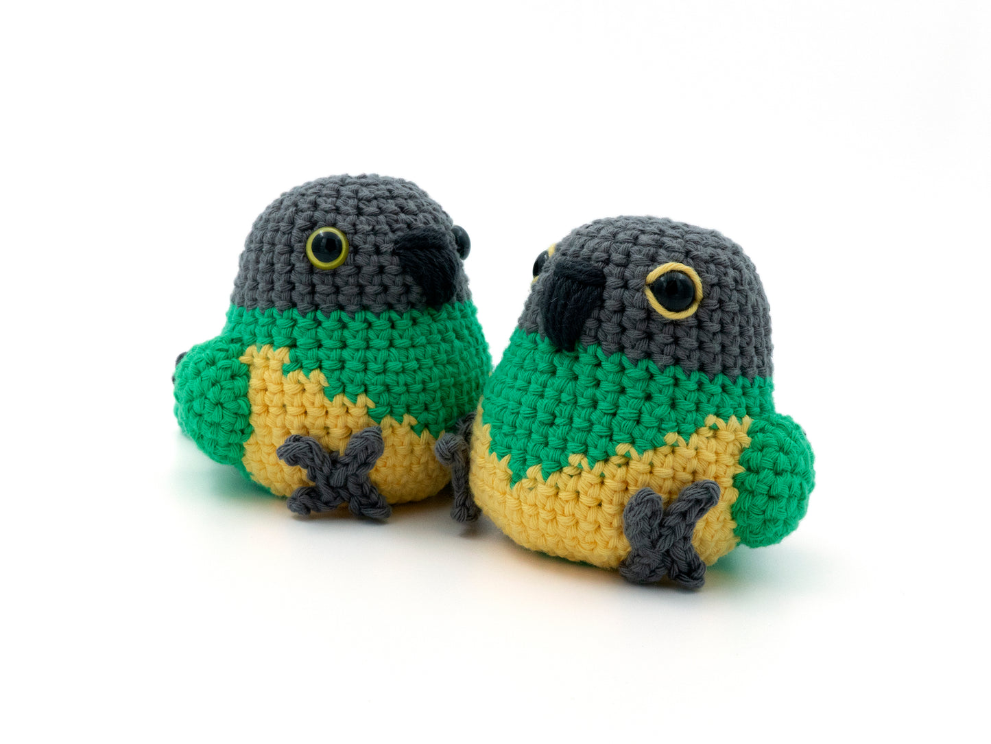 Two crocheted parrot toys in green, yellow, and gray on a white background