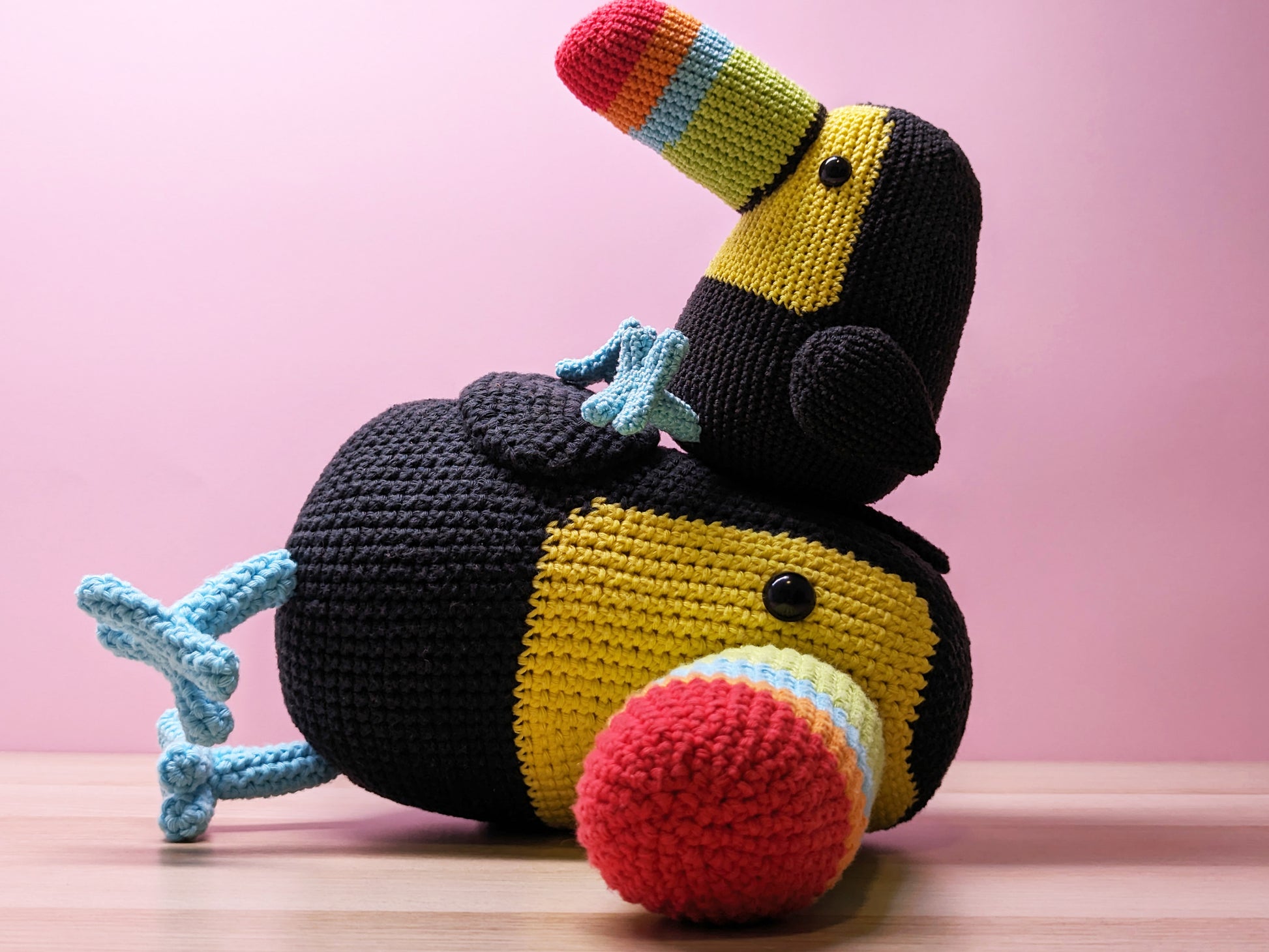 a small crochet toucan sits on top of a large toucan that has fallen over